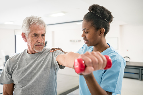 Physiotherapist correcting her senior patient with his shoulder posture as he lifts free weights