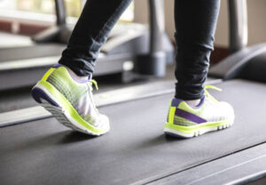 Close up young women walking on treadmill, wearing long black legging.